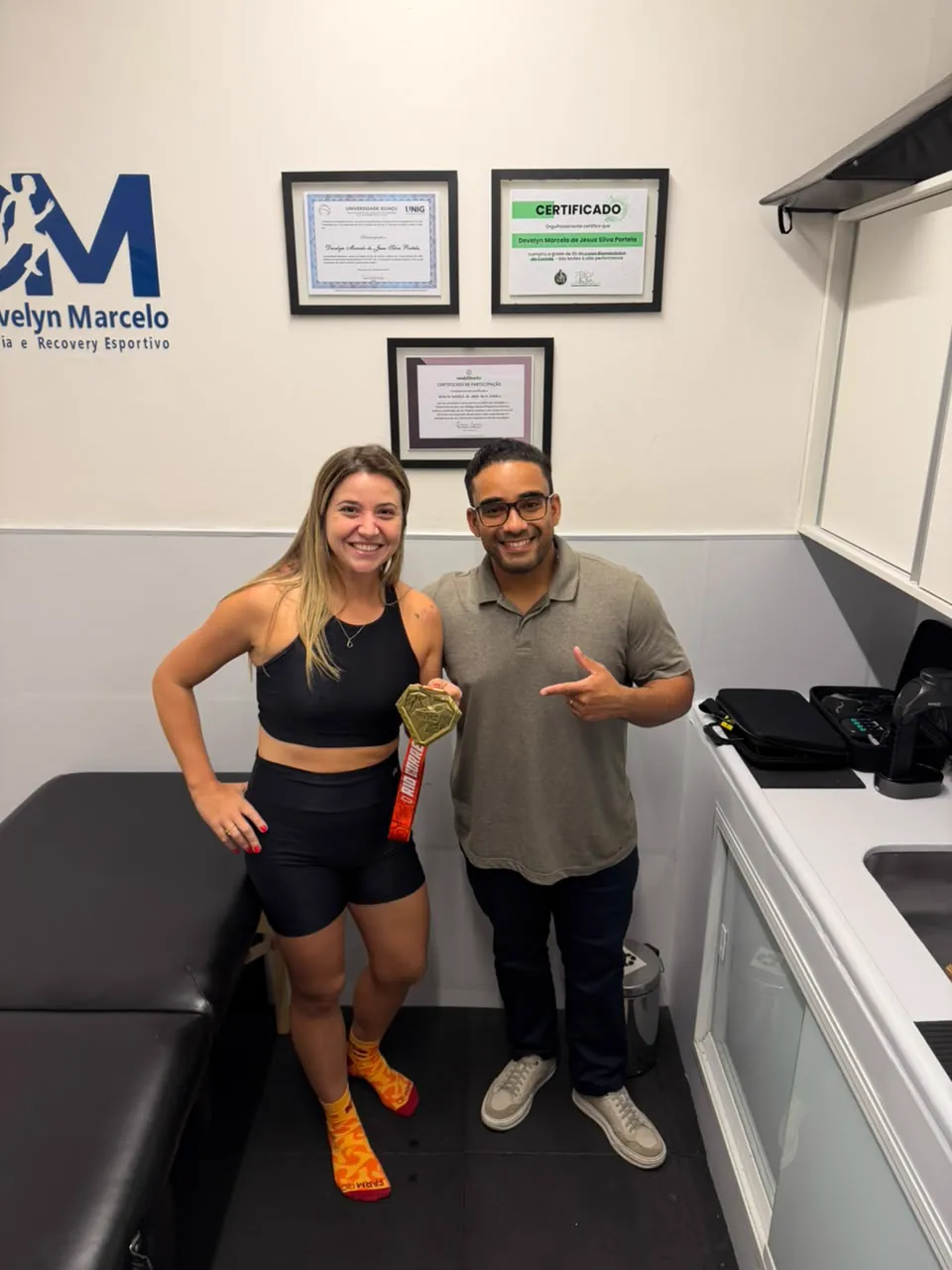 Paciente com medalha do Rio Corre ao lado do Dr. Develyn na sala de atendimento